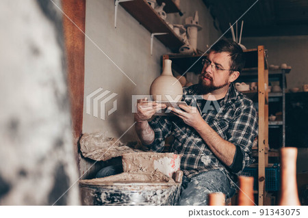Master works on the potter's wheel creating a jug of clay 91343075