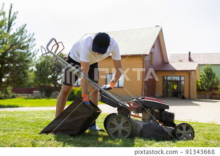 Man disconnects a full grass catcher on a lawn mower Man disconnects a full grass catcher on a lawn mower 91343668