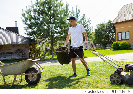 Young guy empties the grass catcher of the lawn mower 91343669