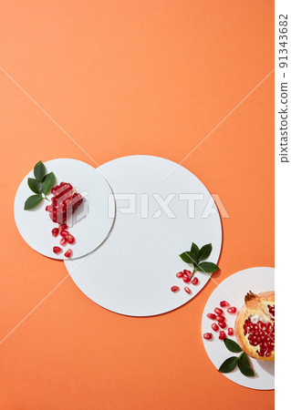 Flatlay Abstract white circle podium on orange background for cosmetics presentation with pomegranate extract. Pomegranate placed next to the product display platform. Top view image. Flatlay Abstract white circle podium on orange background for cosmetics presentation with pomegranate extract. Pomegranate placed next to the product display platform. Top view image. 91343682