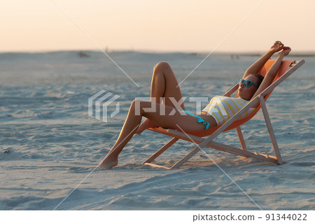 Stylish slim woman in deckchair on shore Stylish slim woman in deckchair on shore 91344022