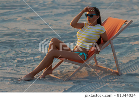 Stylish slim woman in deckchair on shore Stylish slim woman in deckchair on shore 91344024