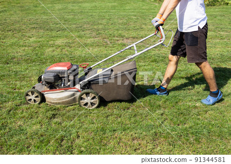 Young man mows the lawn in his yard with a gasoline lawn mower 91344581