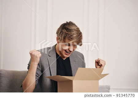 man sitting on the couch and unpacking cardboard box. man sitting on the couch and unpacking cardboard box. 91345770