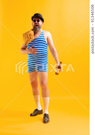 Funny beachgoer, fat funny man wearing retro striped swimsuit and vintage bowler hat posing isolated on bright yellow background. Vacation, summer, humor Funny beachgoer, fat funny man wearing retro striped swimsuit and vintage bowler hat posing isolated on bright yellow background. Vacation, summer, humor 91346506