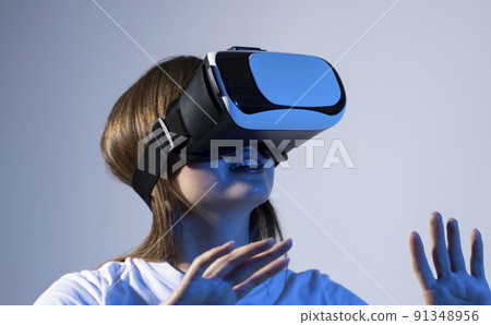 Young brunette woman wearing a virtual reality headset goggles and playing a game with a friends in metaverse. Future technology concept. Young brunette woman wearing a virtual reality headset goggles and playing a game with a friends in metaverse. Future technology concept. 91348956