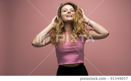 Young woman listening music in headphones and dancing with a smile face and stand over pink background. Attractive lady enjoying song copy space. Young woman listening music in headphones and dancing with a smile face and stand over pink background. Attractive lady enjoying song copy space. 91349057