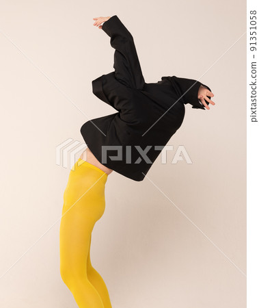 Portrait of girl in yellow tights posing tangled up in black jacket isolated over grey studio background Portrait of girl in yellow tights posing tangled up in black jacket isolated over grey studio background 91351058