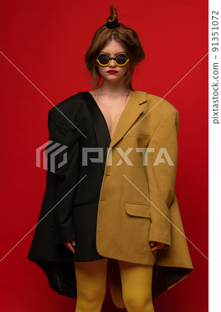 Stylish portrait of young girl wearing two oversized jackets, stylish extravagant glasses, posing isolated over red background Stylish portrait of young girl wearing two oversized jackets, stylish extravagant glasses, posing isolated over red background 91351072
