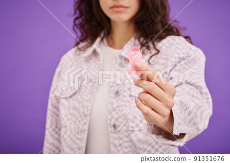 Close-up of young woman holding cancer awareness ribbon against purple background 91351676
