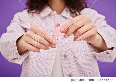 Close-up of woman holding pink breast cancer ribbon against purple background 91351678