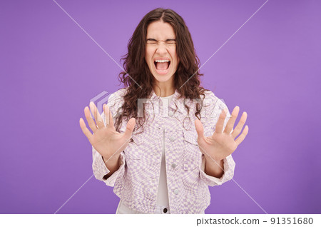 Portrait of young woman screaming with all her might to express emotions standing on purple background 91351680