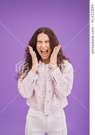 Portrait of young woman expressing her anger and shouting standing against purple background 91351684