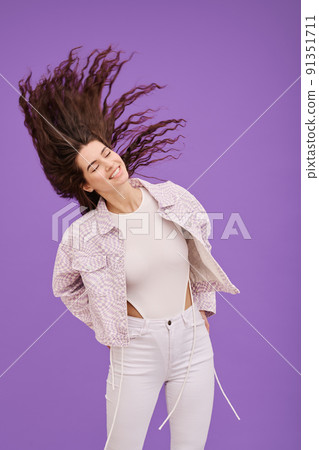 Happy young girl waving her head with long curly hair and smiling standing against purple background Happy young girl waving her head with long curly hair and smiling standing against purple background 91351711