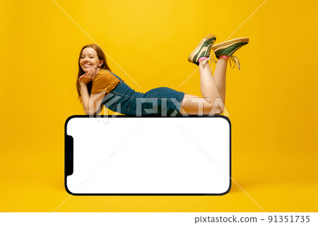 Smiling young girl lying on huge 3d model of cellphone with blank white screen isolated on yellow background, Youth, new app or website, copy space for your ad, mockup Smiling young girl lying on huge 3d model of cellphone with blank white screen isolated on yellow background, Youth, new app or website, copy space for your ad, mockup 91351735