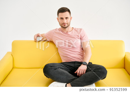 Young man watching TV with remote control sitting on comfort sofa 91352599