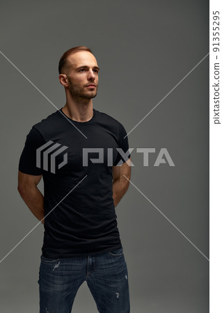 An attractive white man in jeans and black shirts tands in full growth against a gray background. Copy space 91355295