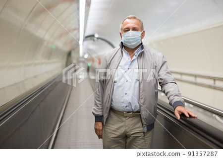 Elderly man in protective mask walks along a travelator in underground metro Elderly man in protective mask walks along a travelator in underground metro 91357287