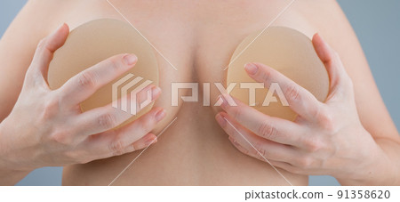 Caucasian naked woman trying on silicone breast implants.  91358620