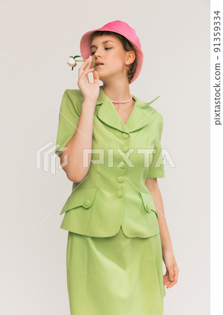 Portrait of young stylish girl in colorful outfit with green suit and pink panama posing isolated over grey studio background Portrait of young stylish girl in colorful outfit with green suit and pink panama posing isolated over grey studio background 91359334