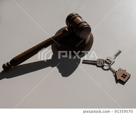 Keys with a keychain in the shape of a house and a judge's gavel on a white background. Keys with a keychain in the shape of a house and a judge's gavel on a white background. 91359570