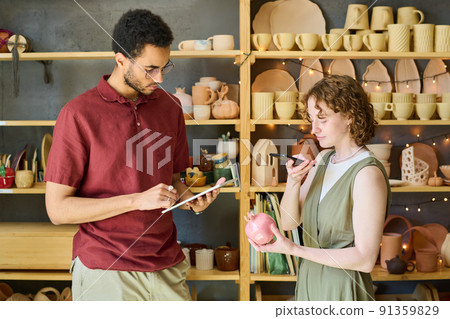 Young female taking photo of pink pomegranate souvenir in front of male clerk 91359829