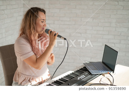 A woman sings into a microphone and shoots a video blog on a laptop 91359890