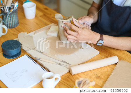 Hands of young male potter forming shape of vase or jug by his workplace Hands of young male potter forming shape of vase or jug by his workplace 91359902