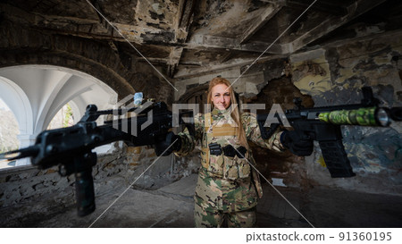 Caucasian woman in army uniform holding two machine guns.  91360195
