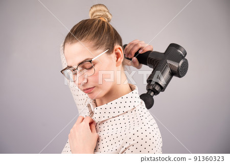 Caucasian business lady makes herself a back massage with a massager gun on a white background. Caucasian business lady makes herself a back massage with a massager gun on a white background. 91360323
