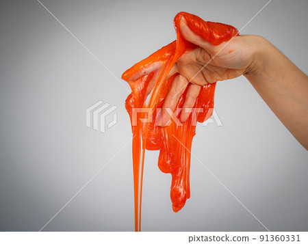 Red slime flowing down from a woman's hand on a white background. Red slime flowing down from a woman's hand on a white background. 91360331