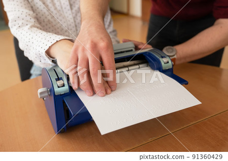 A man teaches a blind woman to type on braille machine.  91360429