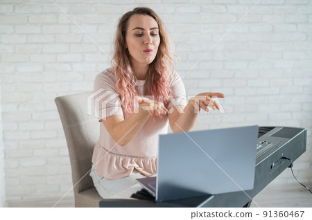 A friendly woman plays the electronic piano and conducts a video blog on her laptop. Stay home. Musical instrument teacher. Distance learning music quarantined. 91360467
