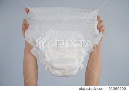 A woman holds an adult diaper on a white background. Incontinence problems. 91360600