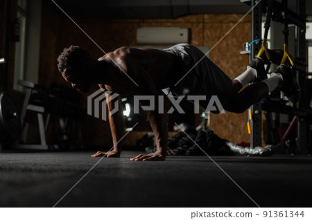 Shirtless afro american man doing exercises with functional loops in the gym. Shirtless afro american man doing exercises with functional loops in the gym. 91361344