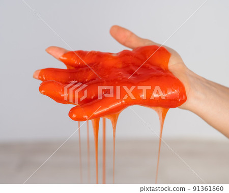 Red slime flowing down from a woman's hand on a white background. Red slime flowing down from a woman's hand on a white background. 91361860