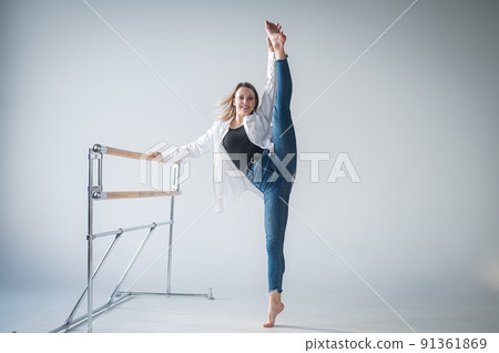 Caucasian woman in casual clothes pulls the longitudinal split at the ballet barre. Caucasian woman in casual clothes pulls the longitudinal split at the ballet barre. 91361869