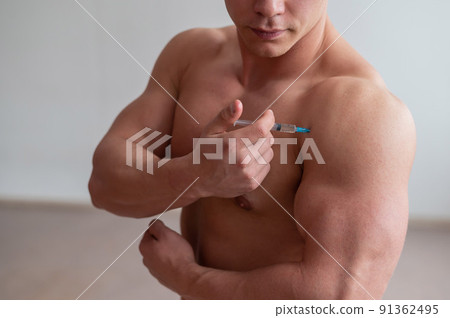 A muscular man with a naked torso holds a dope syringe. Unrecognizable bodybuilder puts himself steroids. Athlete cheats for gaining muscle mass. 91362495