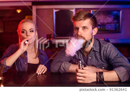 A man and woman smoking electronic cigarette in a vape bar. 91362641