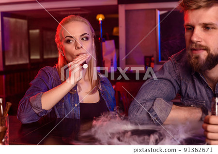 A man and woman smoking electronic cigarette in a vape bar. 91362671