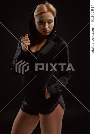 Beautiful seductive sporty girl with the slim sexy figure in the black hoodie, sport underwear and little black shorts is posing in the studio Beautiful seductive sporty girl with the slim sexy figure in the black hoodie, sport underwear and little black shorts is posing in the studio 91362914