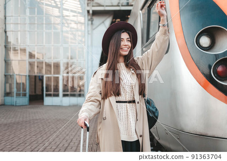 Beautiful traveler waves her hand while standing at the railway station against the background of a train. Beautiful traveler waves her hand while standing at the railway station against the background of a train. 91363704