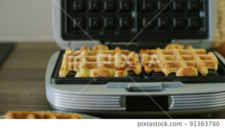 Woman hand opens the waffle iron on the table. Baking waffles in a waffle iron. Breakfast concept. Woman hand opens the waffle iron on the table. Baking waffles in a waffle iron. Breakfast concept. 91363780