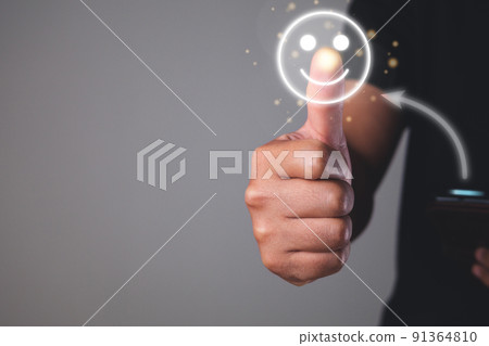 Evaluation and satisfaction concept. Thumb finger points to smile emotion. He sends good emoji to someone by smart phone. Close up shot on grey background. Evaluation and satisfaction concept. Thumb finger points to smile emotion. He sends good emoji to someone by smart phone. Close up shot on grey background. 91364810