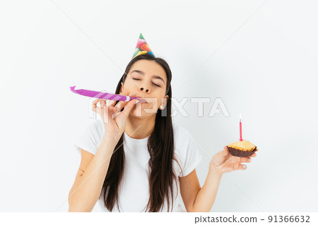 Birthday celebration, young woman in party cap blowing kazoo 91366632