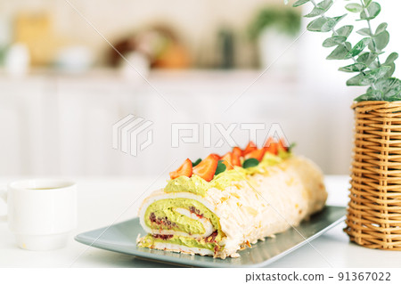 Meringue roll with strawberries on a white table near the basket 91367022