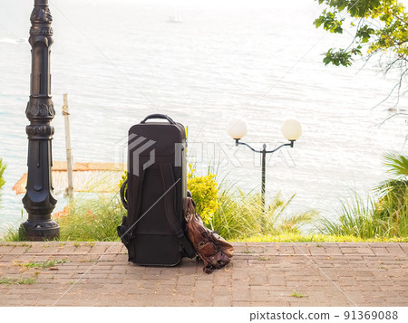A travel suitcase stands on paving slabs against the backdrop of the sea on a summer day. Southern holidays. 91369088