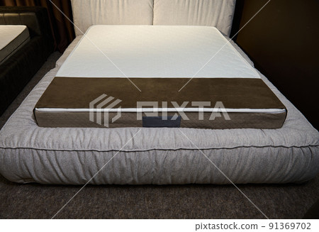 Sylish soft sleeping bed made of a beige upholstery with orthopedic mattress displayed for sale in furniture showroom. Bedroom design 91369702