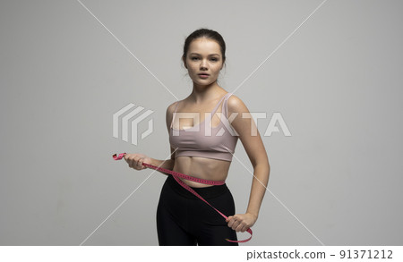 Attractive young brunette women in sportswear and takes measurements of her waist. Measurements of a body. Sport, fitness and diet. 91371212