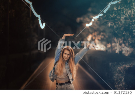 A woman walks, waving her arms above her head, along a night alley in the park. Blurred image 91372180